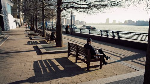 Free People enjoying a sunny day on a riverside promenade with benches and trees by the river. Stock Photo