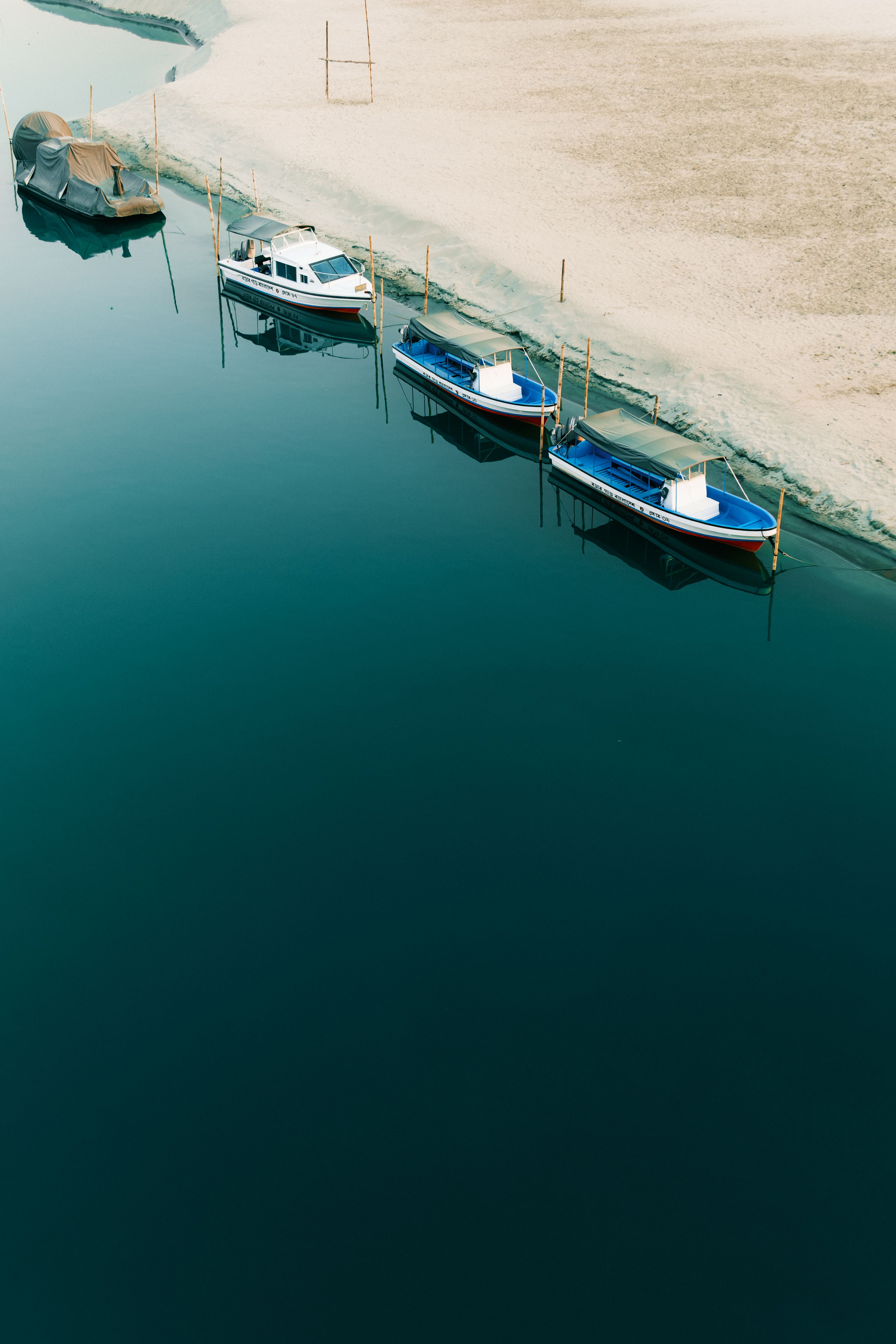 A serene view of boats docked on a calm river in Kurigram, Bangladesh, under a clear summer sky.