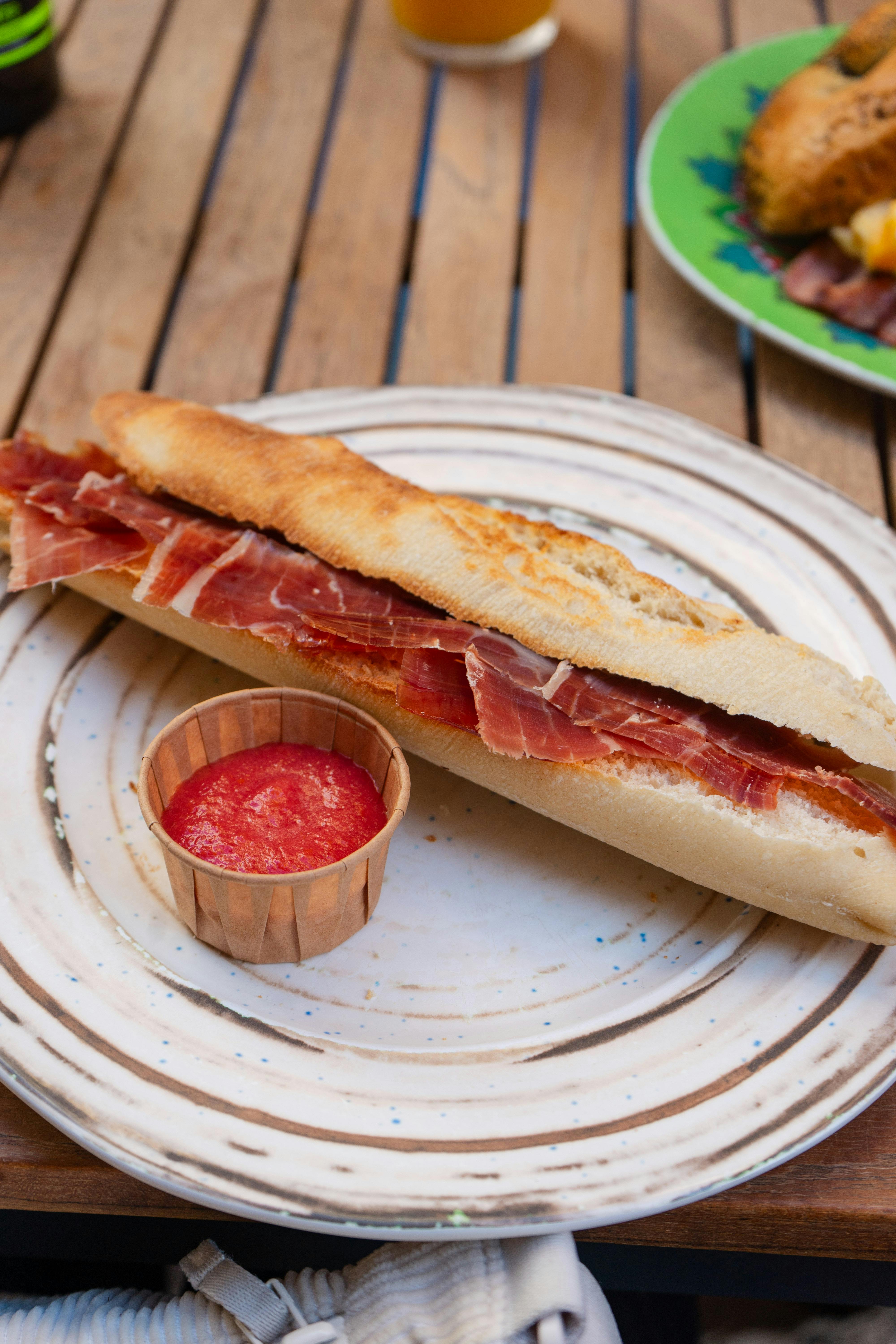 Delicious Spanish bocadillo with jamón and tomato sauce served on a rustic plate outdoors.