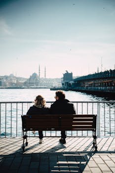A couple sits on a bench by the Istanbul waterfront, enjoying the picturesque cityscape.