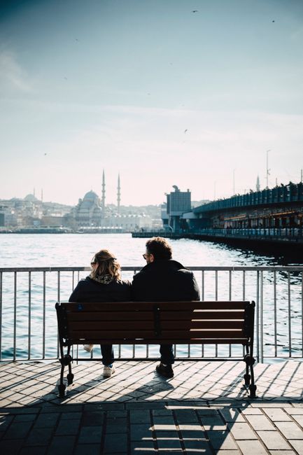 A couple sits on a bench by the Istanbul waterfront, enjoying the picturesque cityscape.