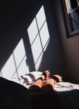 Feet resting on bed with sunlight casting window shadows on the wall. Calm morning indoors.