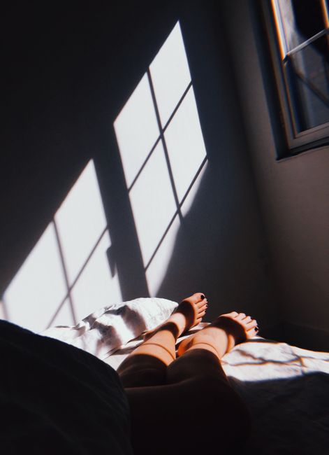 Feet resting on bed with sunlight casting window shadows on the wall. Calm morning indoors.