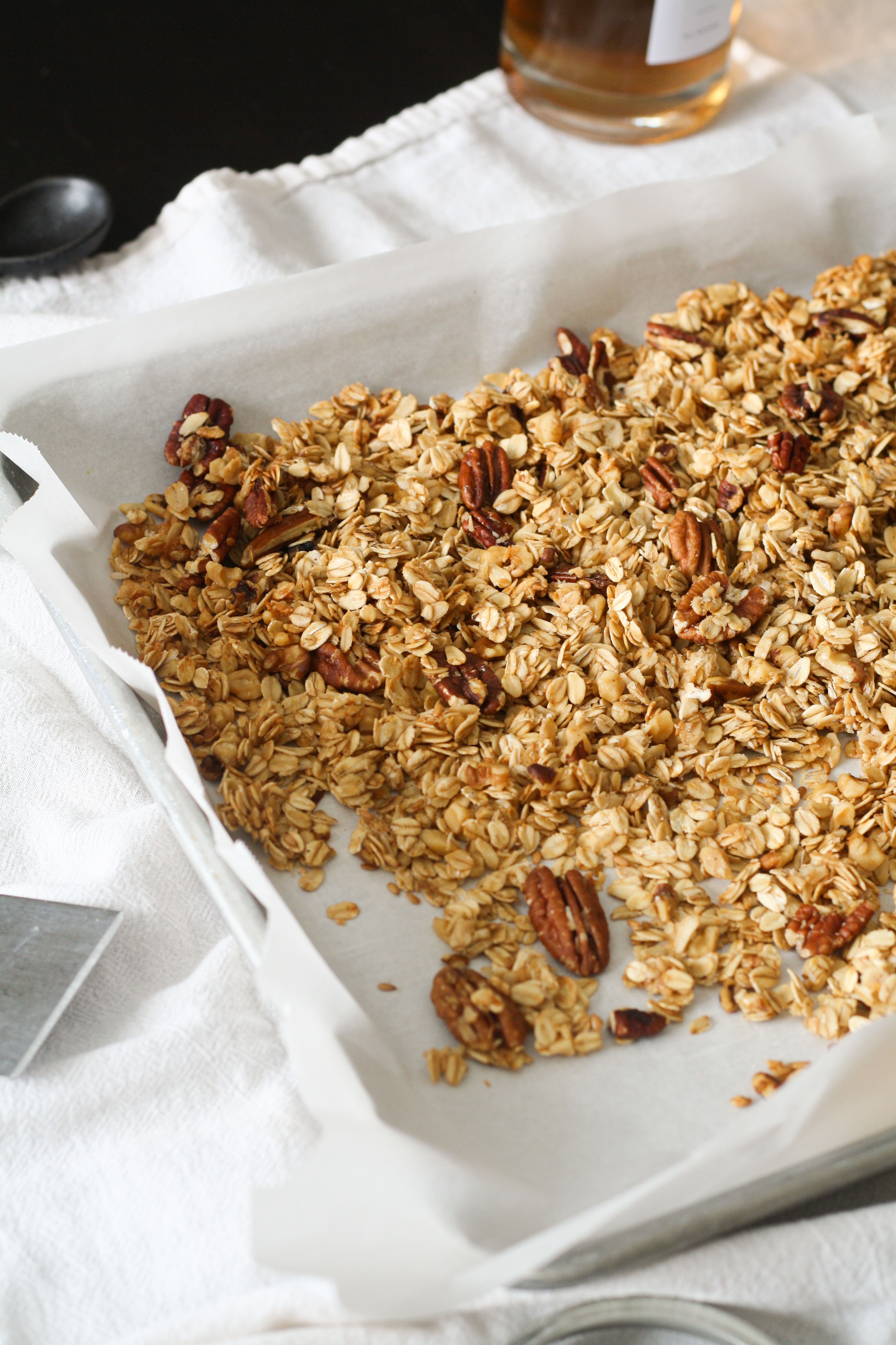 Golden-brown granola clusters cooling on a parchment-lined sheet pan, with toasted oats, almonds, and dried cranberries visible.