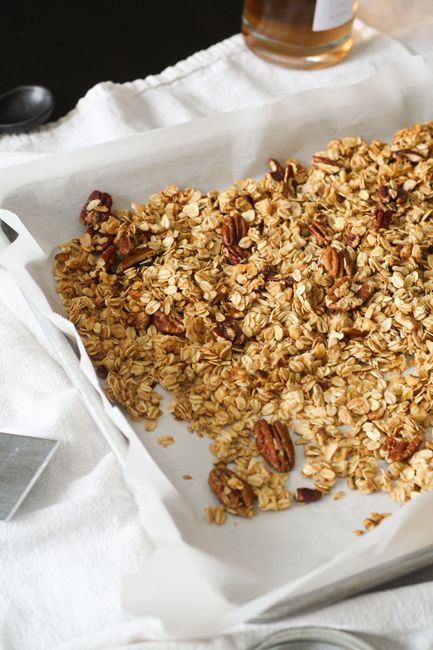Golden-brown granola clusters cooling on a parchment-lined sheet pan, with toasted oats, almonds, and dried cranberries visible.