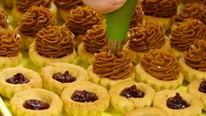 Close-up of pastry tarts being filled with caramel and jam on a tray.