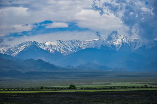 Free A breathtaking view of snow-capped mountains with lush green fields in the foreground. Stock Photo
