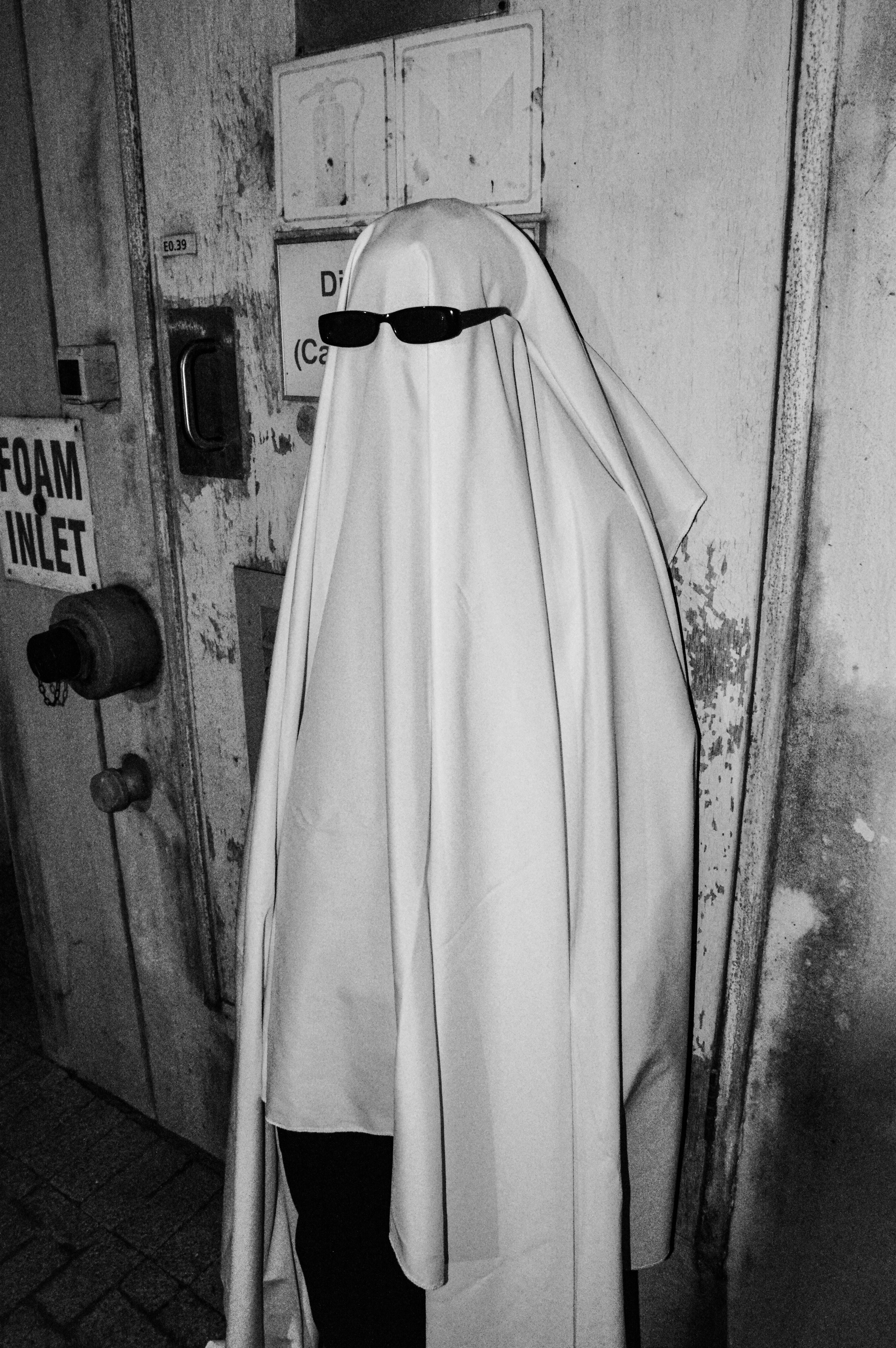 A person dressed as a ghost in sunglasses stands in an urban area.