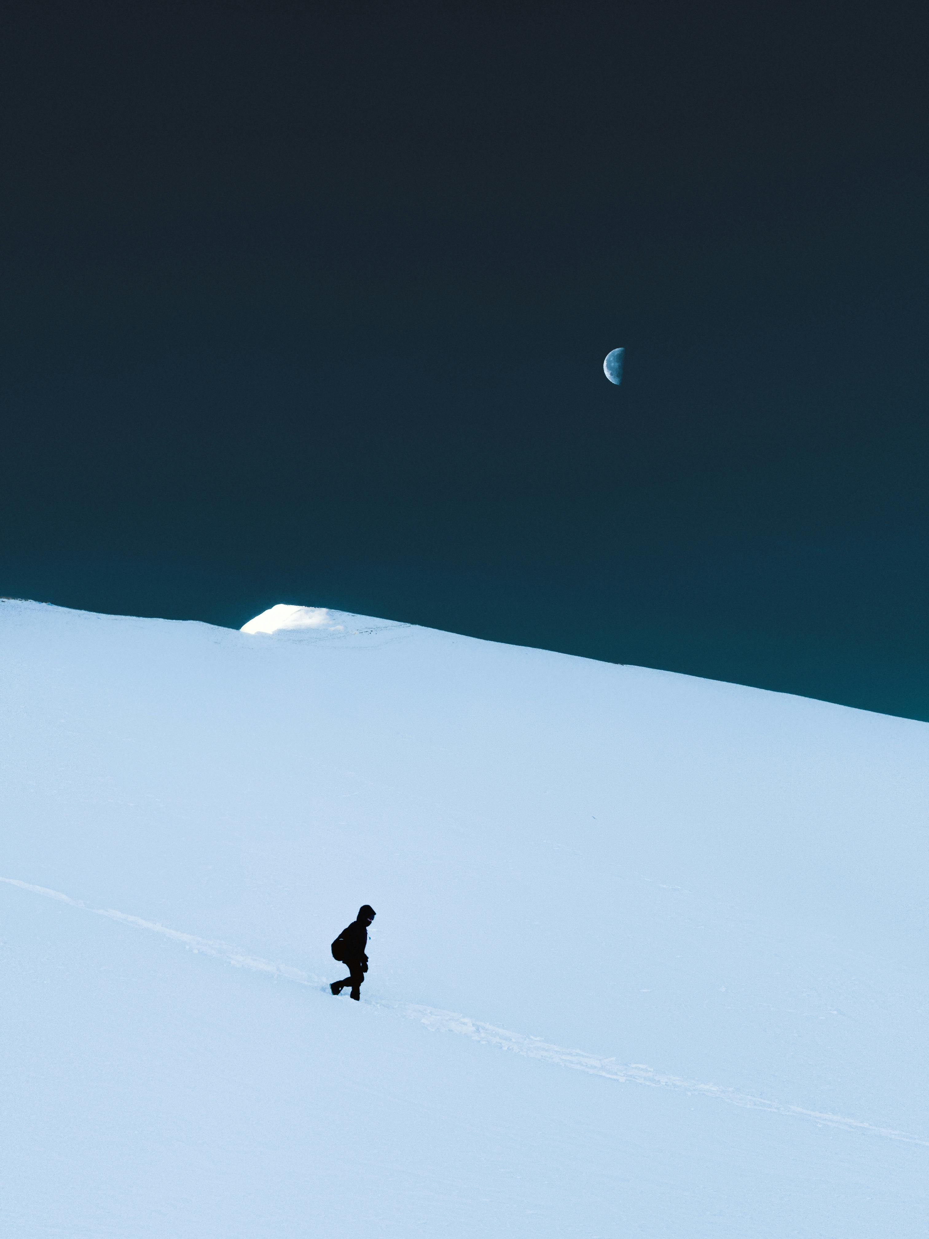 A solitary figure hikes through snowy hills under a serene moonlit night in Veneto, Italy.