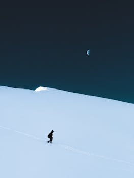 A solitary figure hikes through snowy hills under a serene moonlit night in Veneto, Italy.