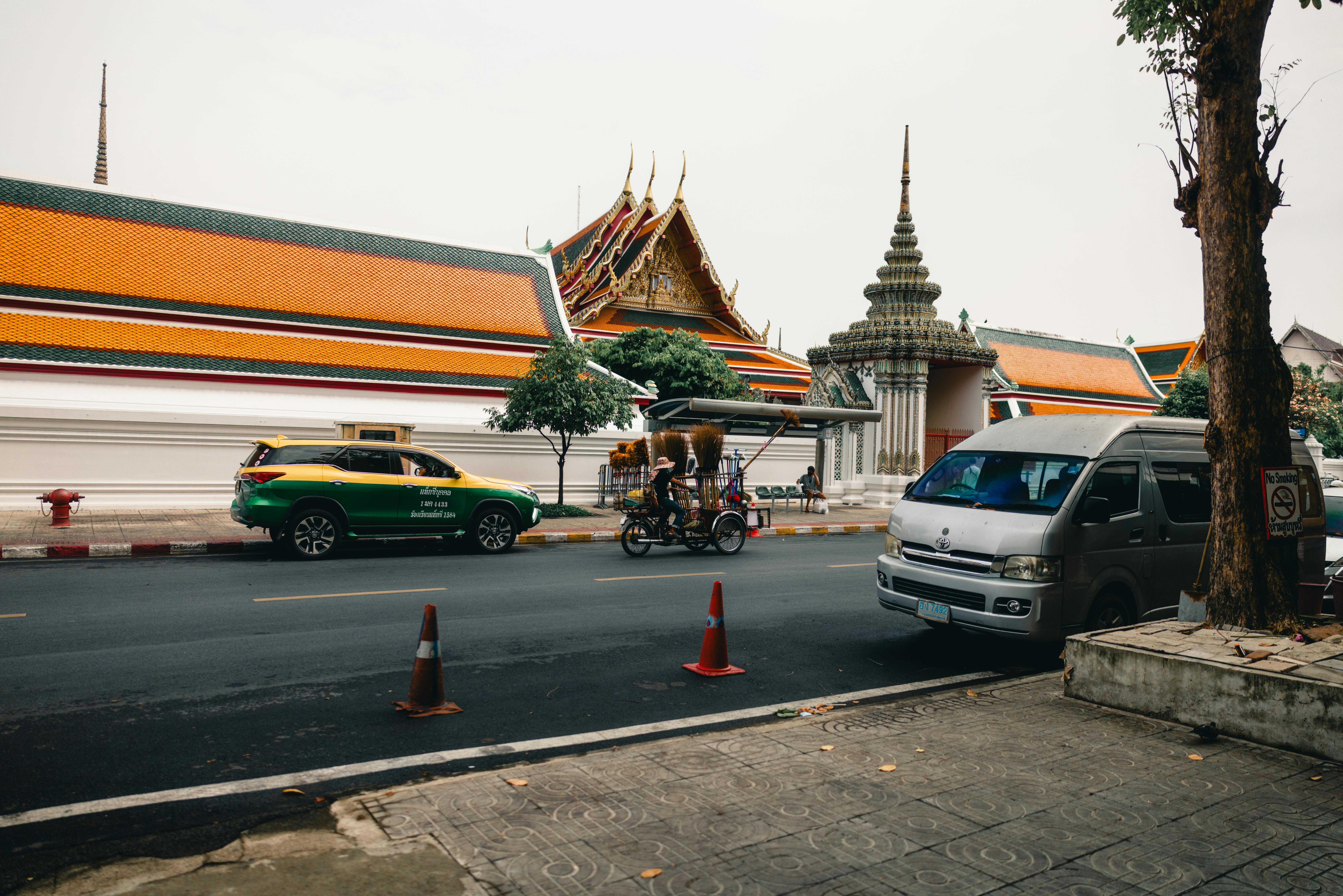A bustling street in Bangkok featuring a temple, local vehicles, and vibrant colors.