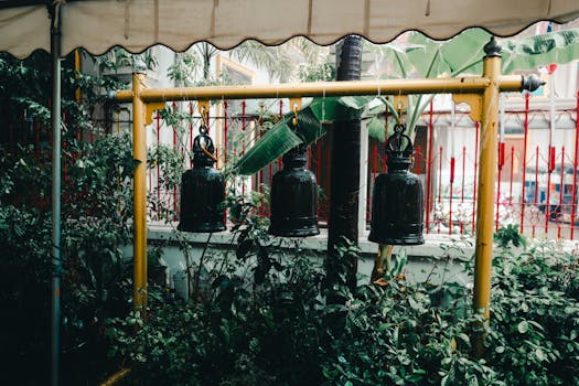 Traditional bells hanging in a lush garden in Bangkok, Thailand, creating a serene atmosphere.