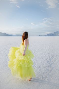 A woman in a vibrant yellow dress stands elegantly on vast salt flats under a serene sky.
