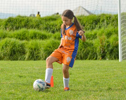 Girl playing soccer in orange team uniform on a grassy field.