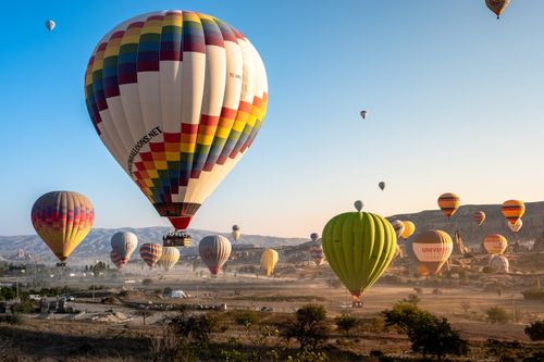 Free Vibrant hot air balloons soar over Cappadocia's unique landscape at sunrise, creating a stunning aerial view. Stock Photo