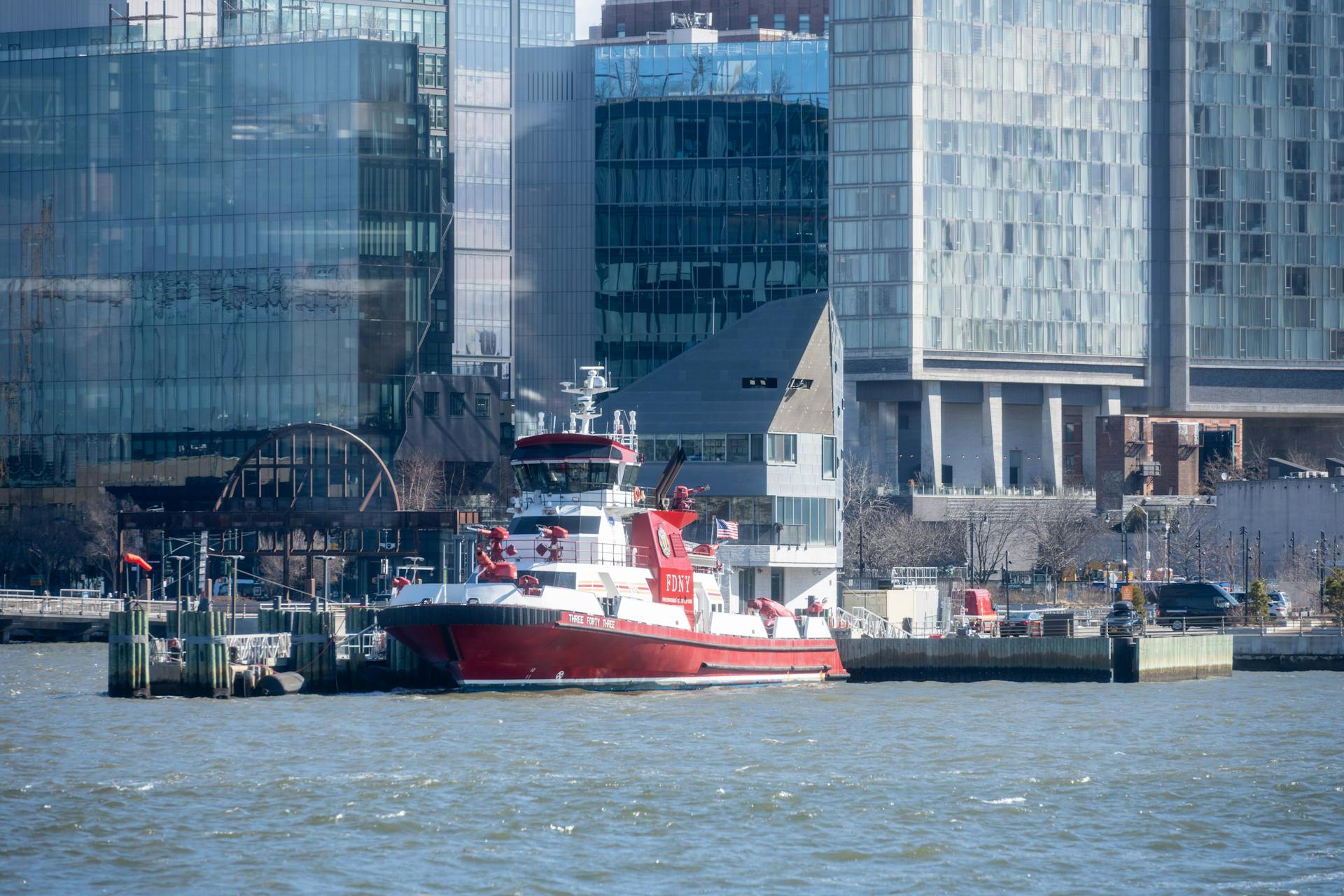 Fireboat in New York City harbor with modern glass buildings in the background.