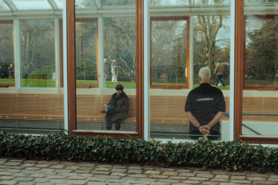 A thoughtful scene with a person reflecting through large glass windows in a modern setting.