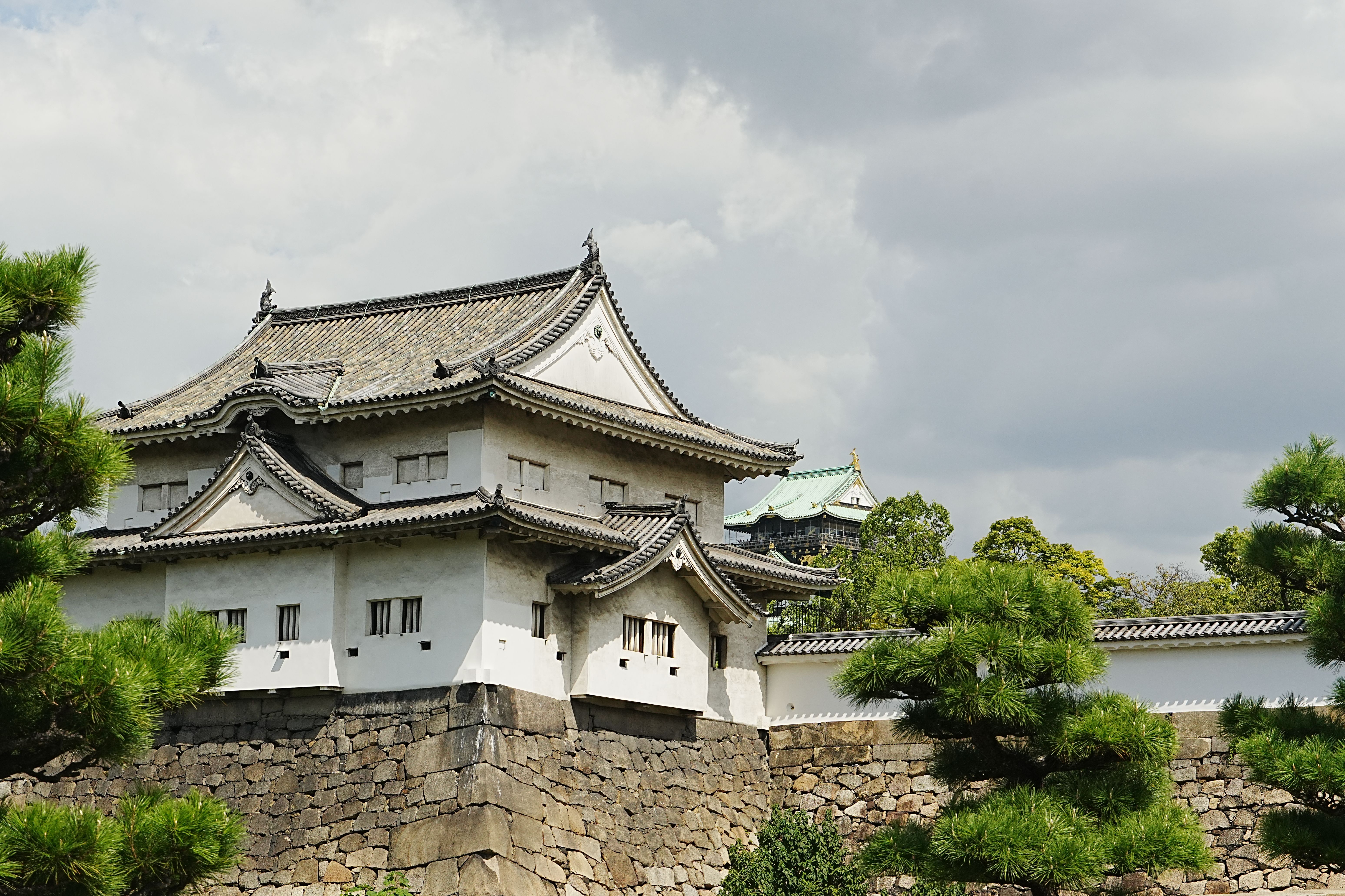Beautiful exterior of Osaka Castle surrounded by lush trees under a cloudy sky, showcasing traditional Japanese architec