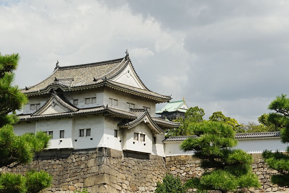 Beautiful exterior of Osaka Castle surrounded by lush trees under a cloudy sky, showcasing traditional Japanese architec