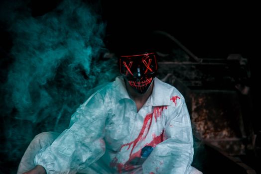 A person in a bloody costume and LED mask surrounded by eerie smoke, depicting a Halloween theme.