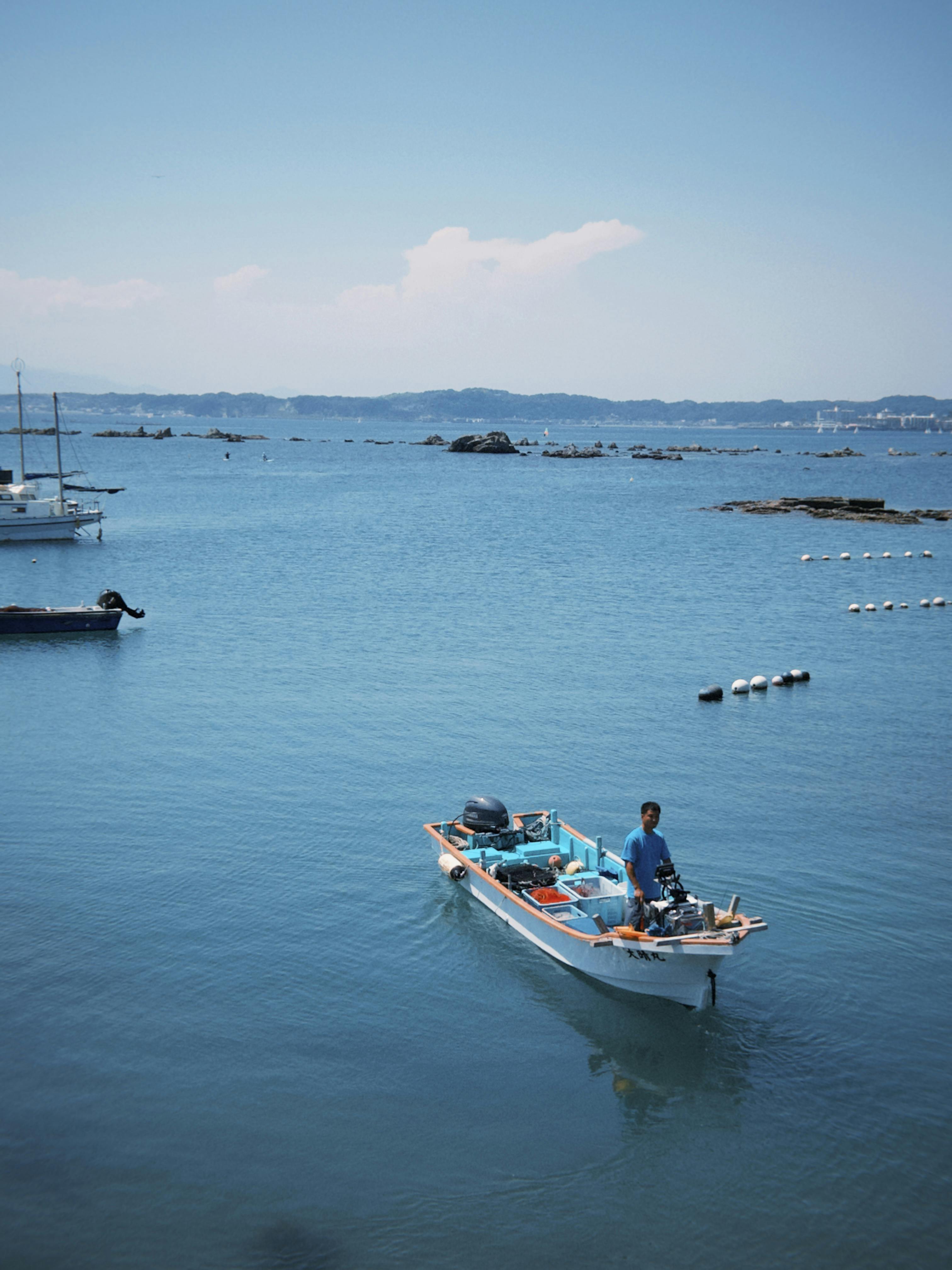 A fisherman navigates his small boat across a calm, blue sea under a clear sky.