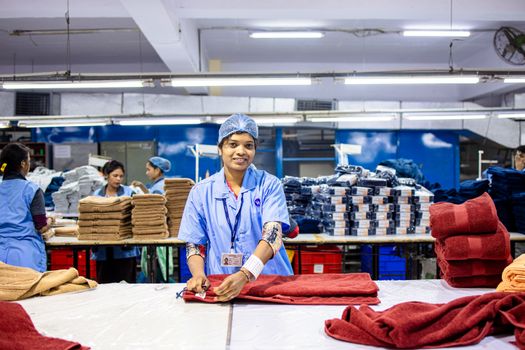 Portrait of a smiling textile worker folding fabrics in a bustling factory environment.