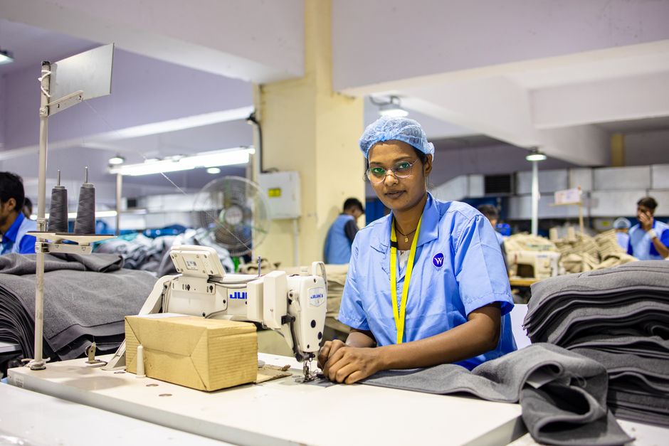 Female textile worker sewing fabric in an Indian factory setting.