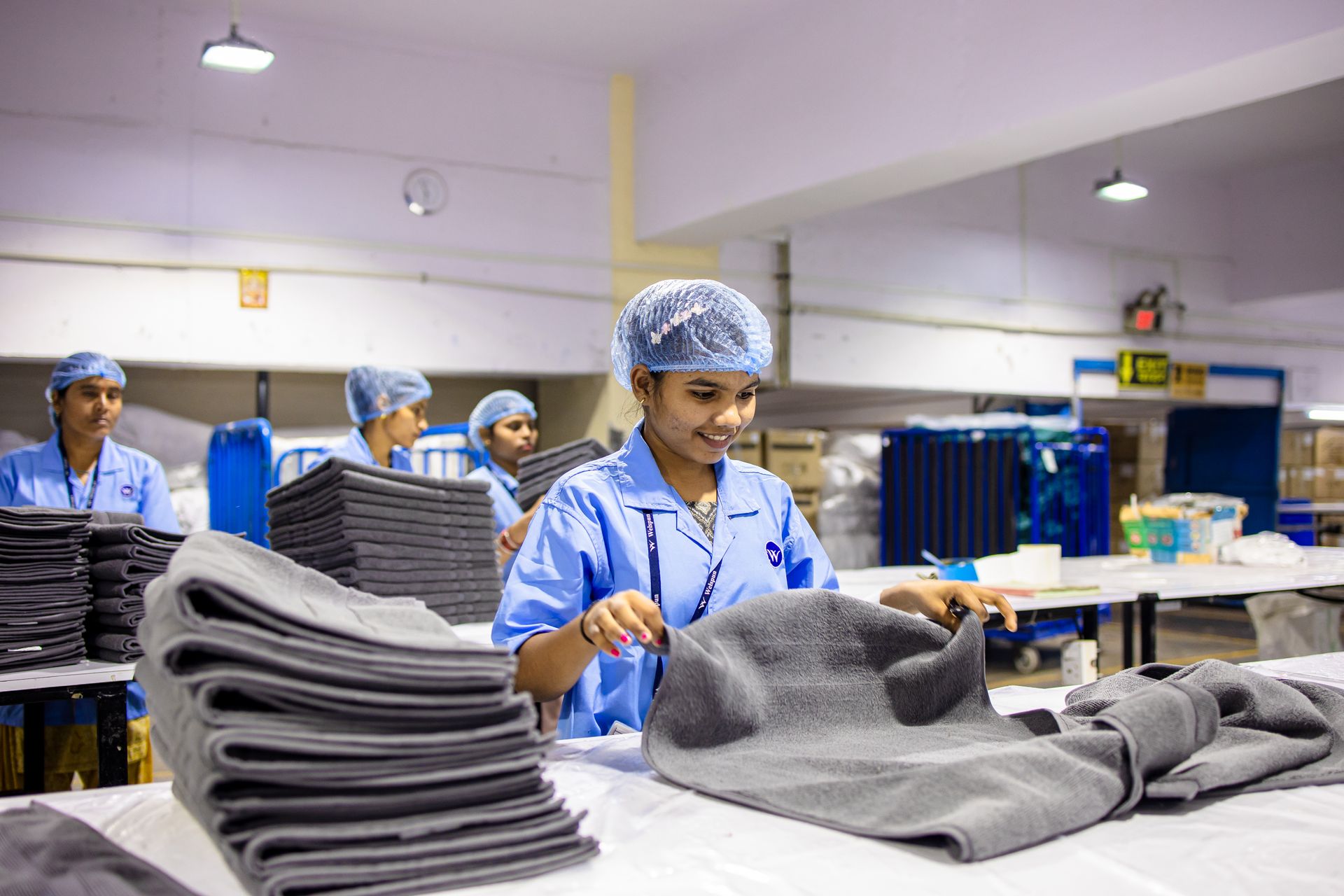 Smiling Indian factory workers folding textiles in a modern facility.