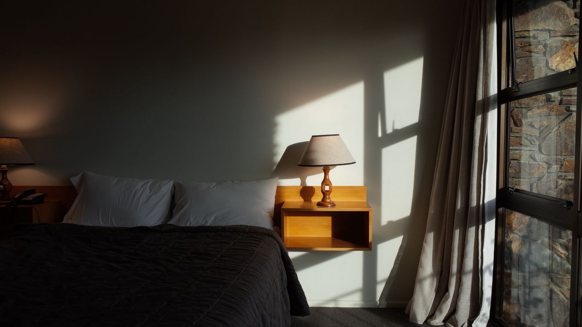 Sunlight softly illuminating a cozy bedroom with a neatly made bed and lamp.