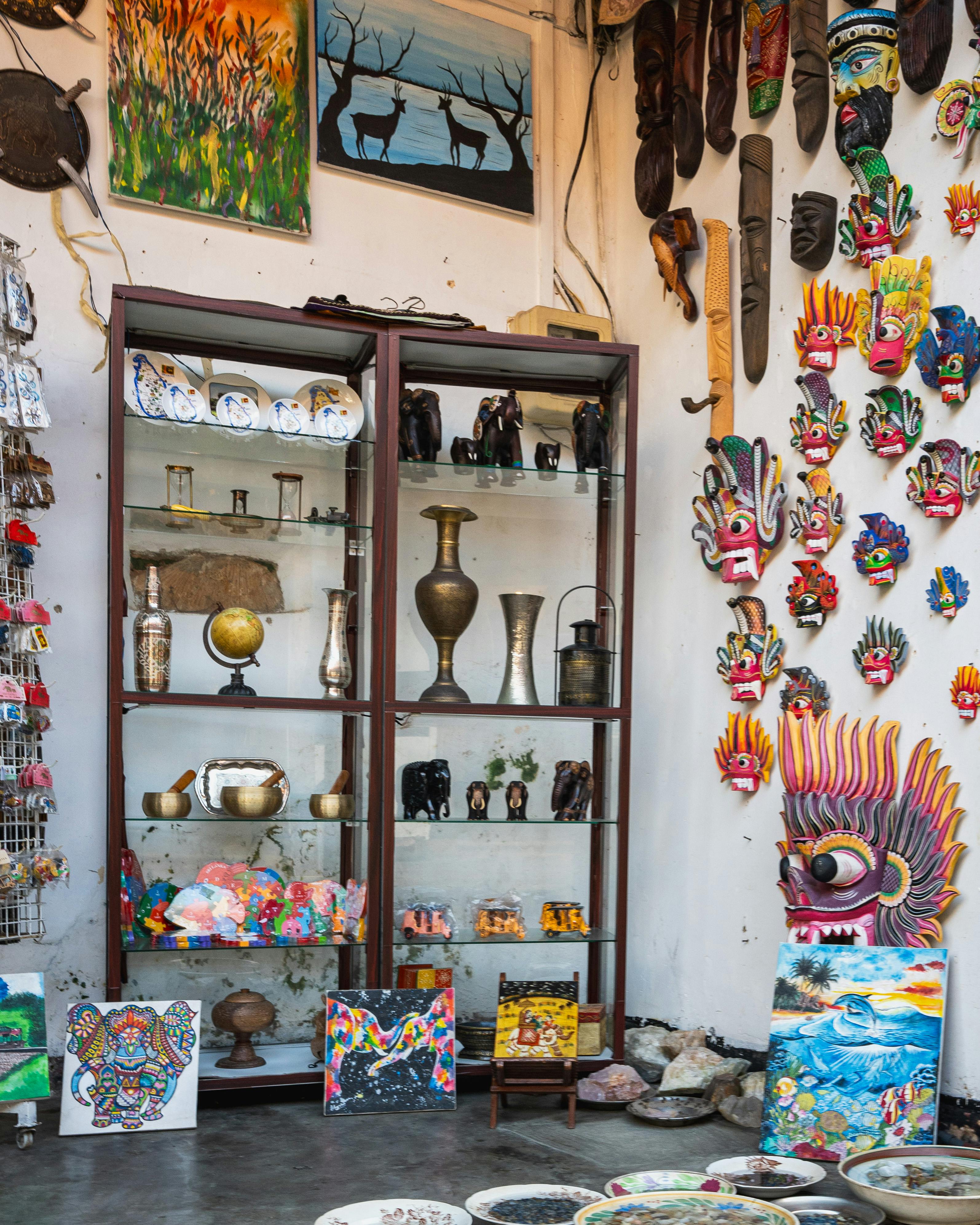 Rows of Balinese paintings and hand-carved wooden masks displayed at a stall in the Ubud Art Market, Bali