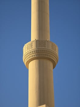 Detailed architectural view of a minaret in Dubai with intricate designs against a clear blue sky.