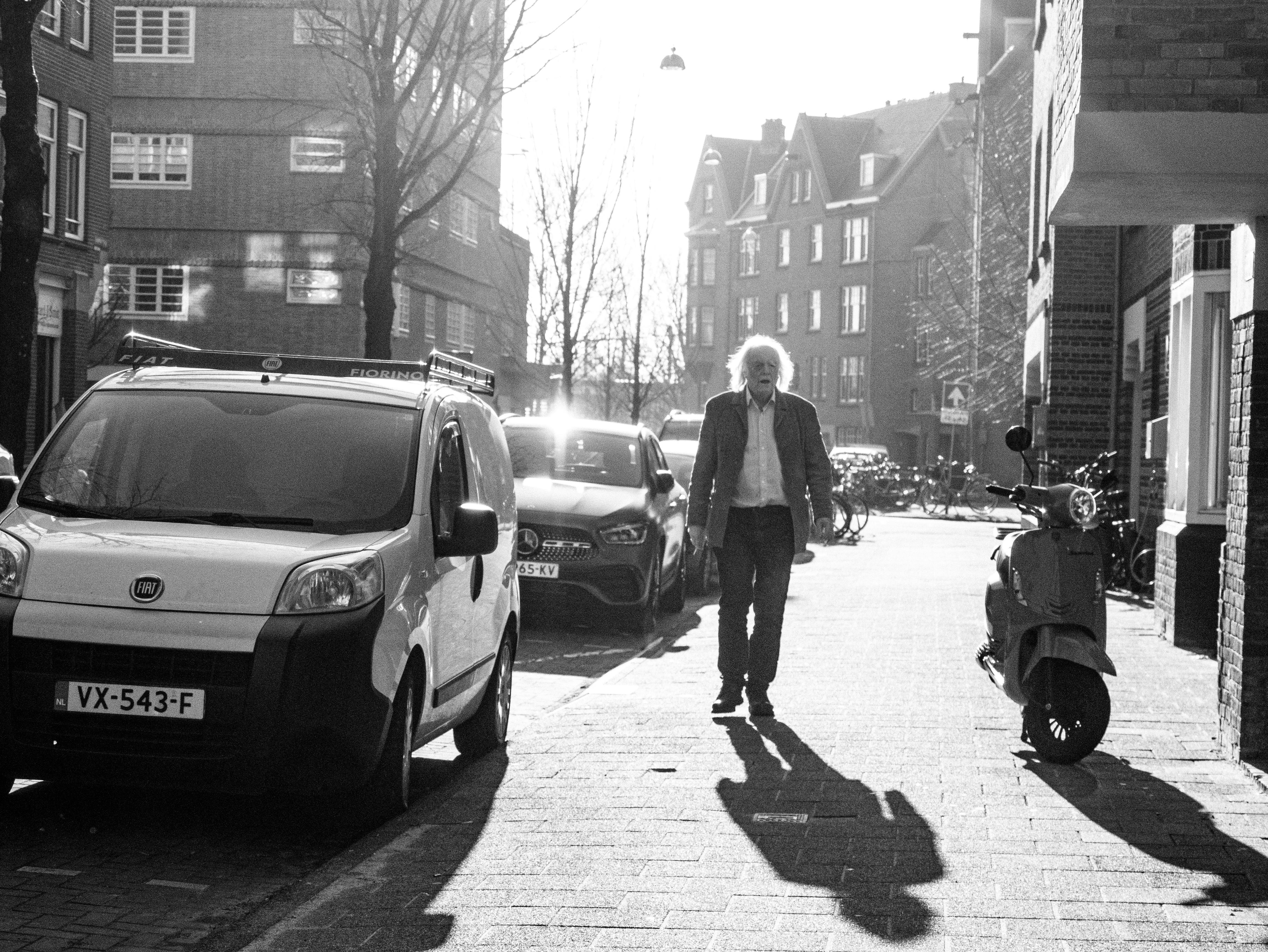 Black and white photo of an elderly man walking on a sunlit street in Amsterdam.