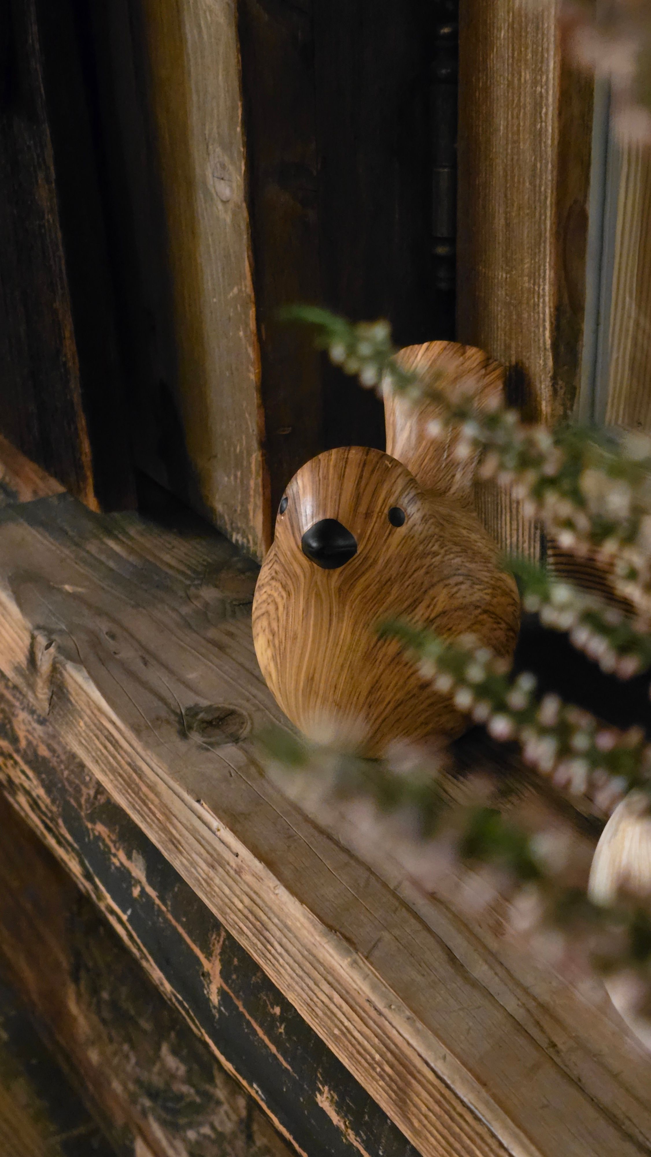 Rustic wooden bird sculpture with natural texture on a wooden shelf indoors.