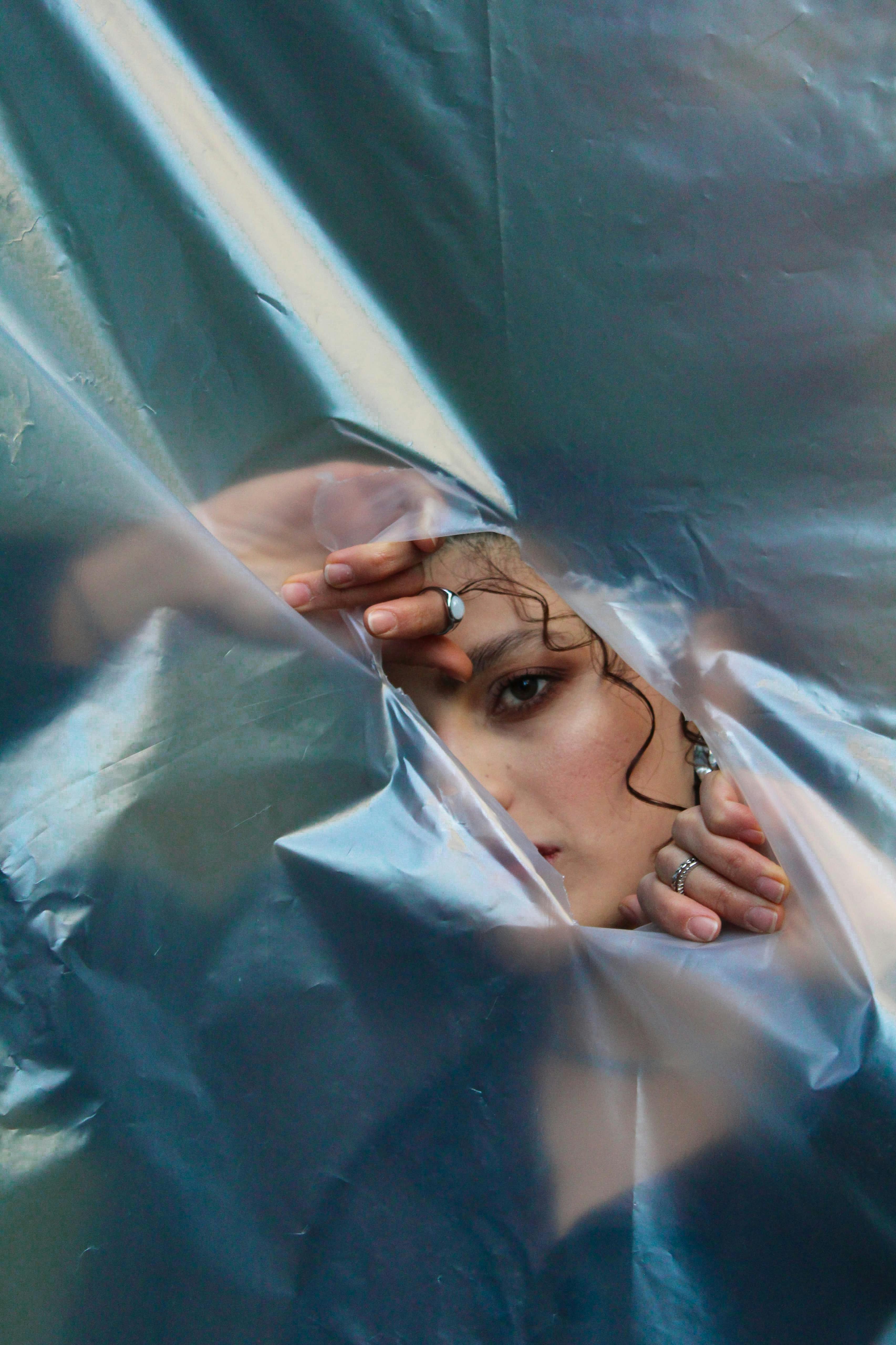 A mysterious and artistic portrait peeks through crinkled plastic wrap, conveying a surreal expression.