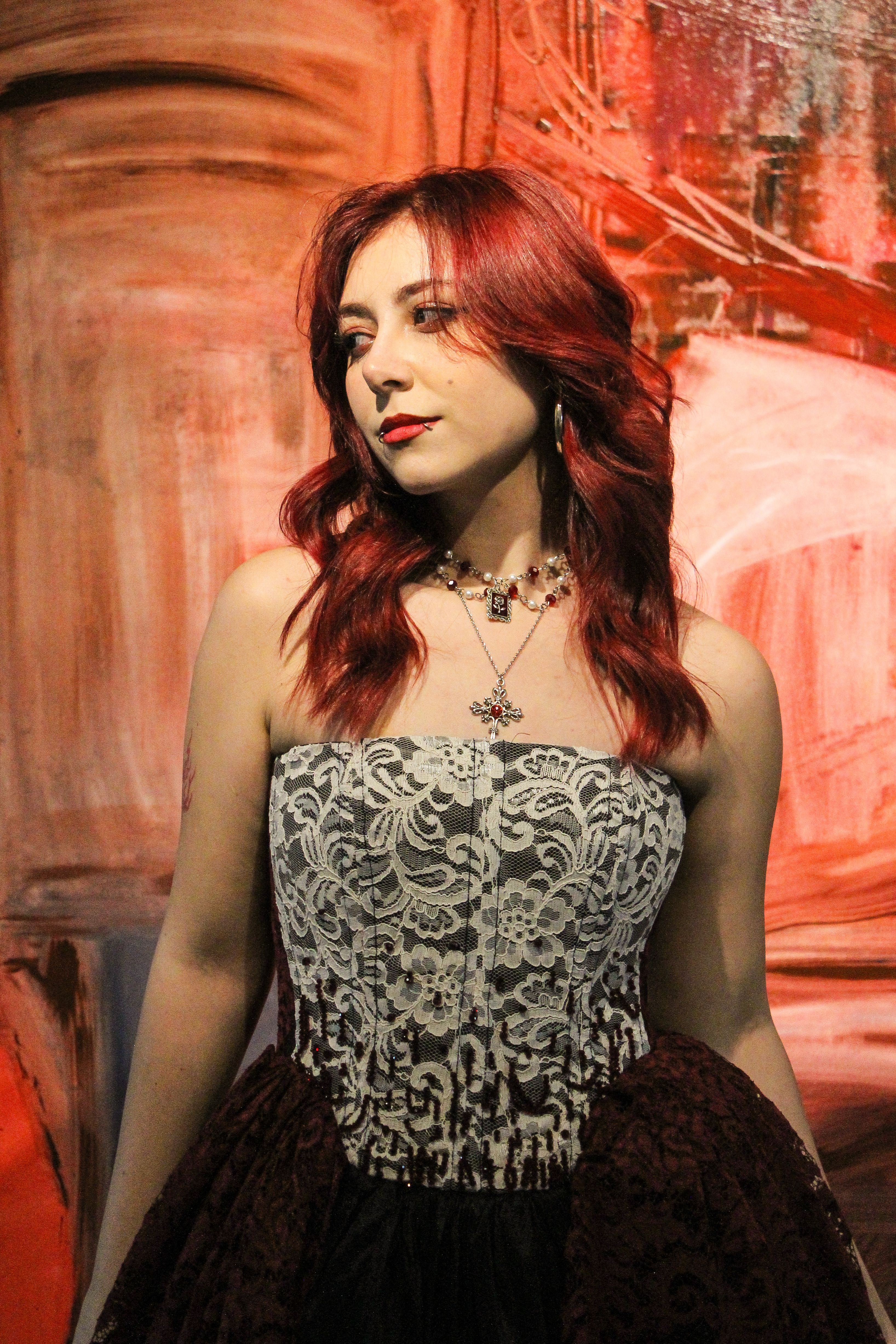 Portrait of a stylish woman with red hair wearing a lace dress in front of an abstract background.