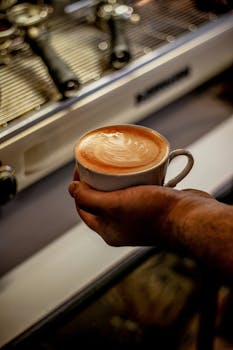 Close-up of a barista holding a coffee cup with heart-shaped latte art in a café in Kermanshah, Iran.