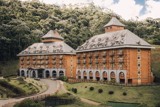 A picturesque Bavarian-style hotel surrounded by lush greenery and forest hillside.