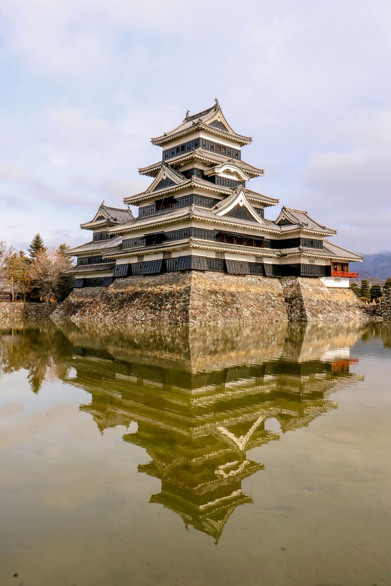 Black Japanese castle keep with reflection in moat — the distinctive dark-timber architecture of Japan's original castle keeps, as seen in Matsue's National Treasure castle