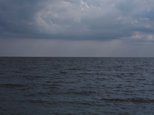 Free A moody seascape view with dark clouds hovering over a calm ocean horizon under a dramatic sky. Stock Photo