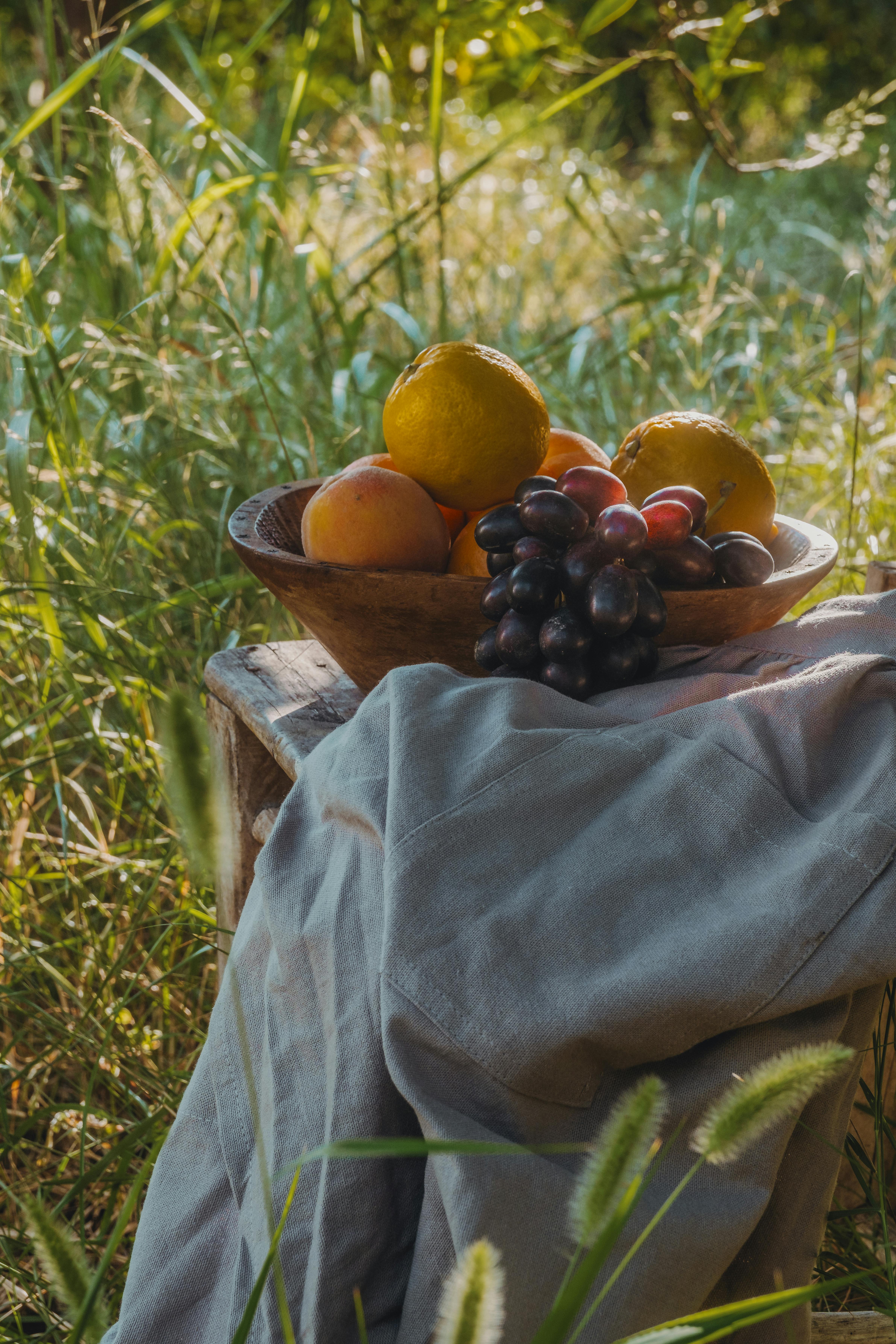 A wooden bowl of assorted fruits in a sunlit garden, conveying warmth and freshness.