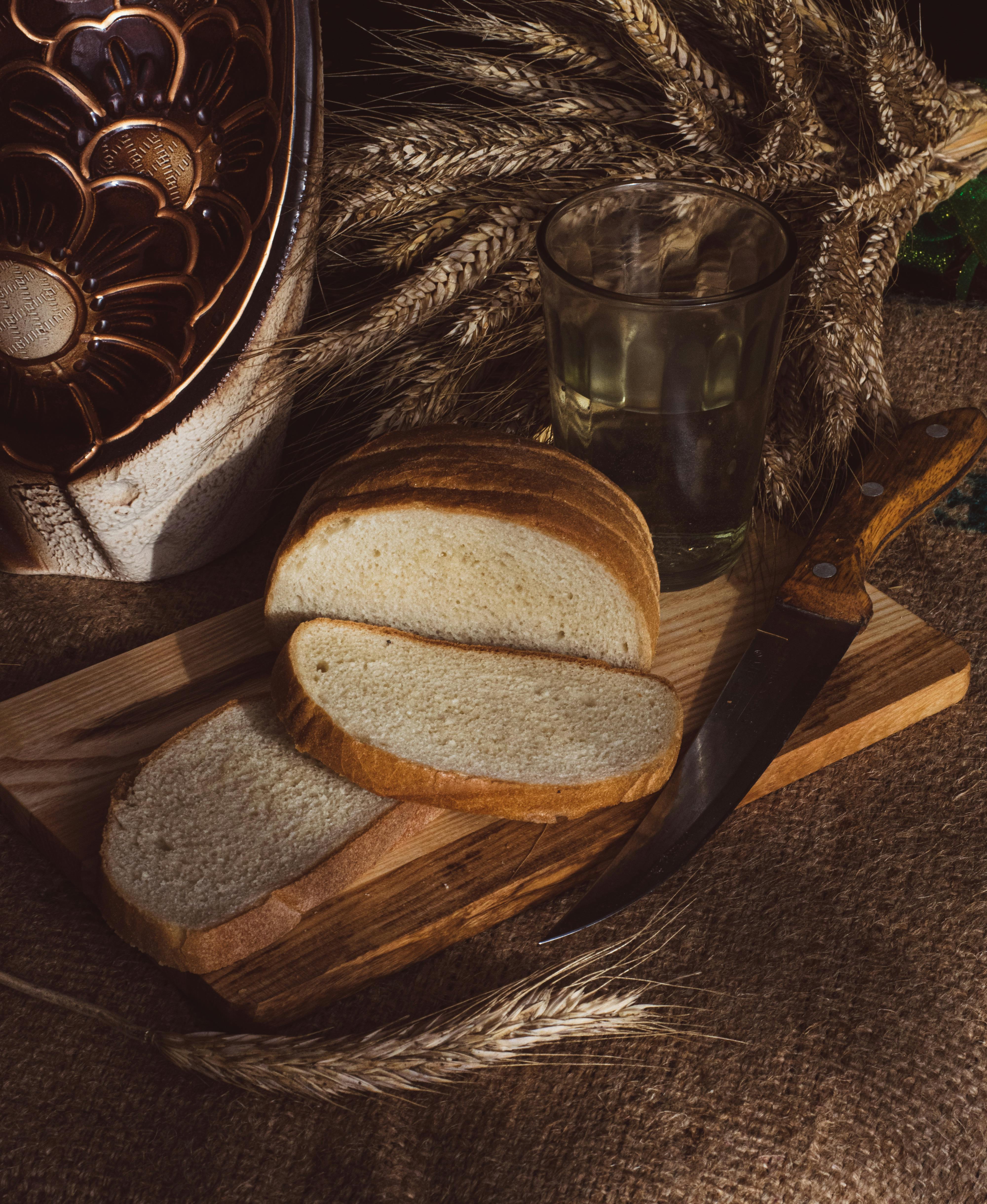 A loaf of bread on a wooden board with wheat stalks and a vintage glass, evoking a rustic feel.
