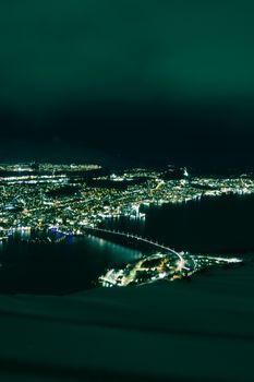 Captivating nighttime aerial view of Tromsø, Norway, showcasing city lights and the Northern Lights.
