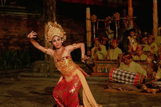 Balinese dancer in vibrant attire performing a cultural dance with musicians in Bali, Indonesia.