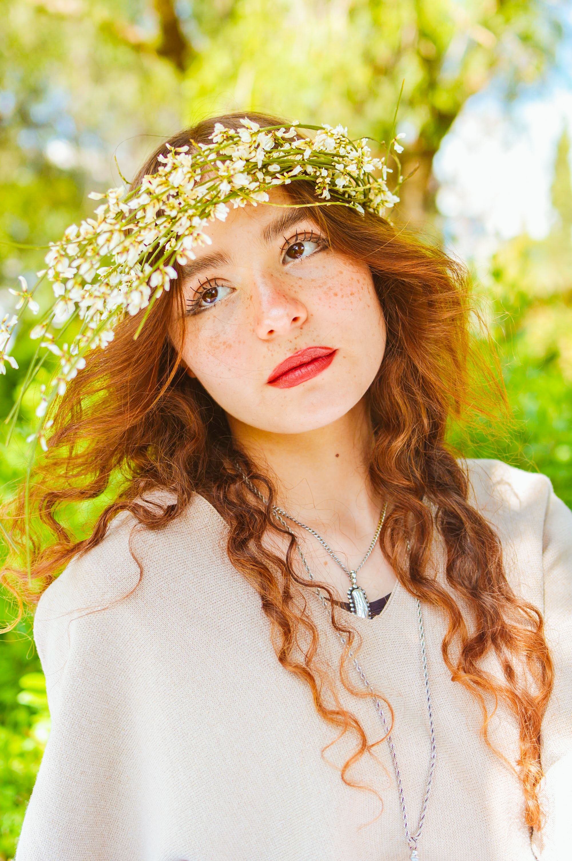 Portrait of a young woman wearing a floral crown, outdoors in a sunny setting.