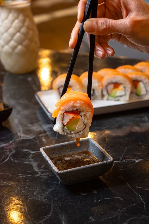 Free Delicious sushi roll being dipped into soy sauce with chopsticks on a table. Stock Photo