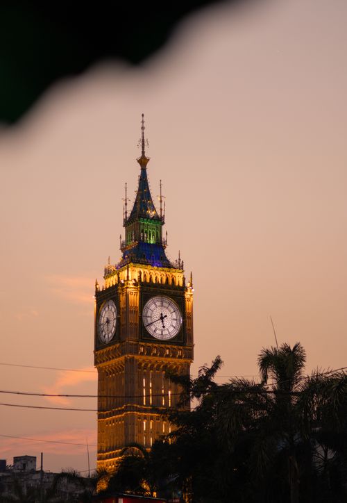 Free Elegant clock tower glowing at dusk with palm trees silhouette. Stock Photo