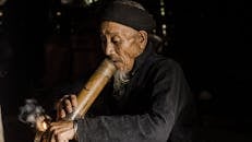 一位老人抽着竹管、冒着烟的特写镜头