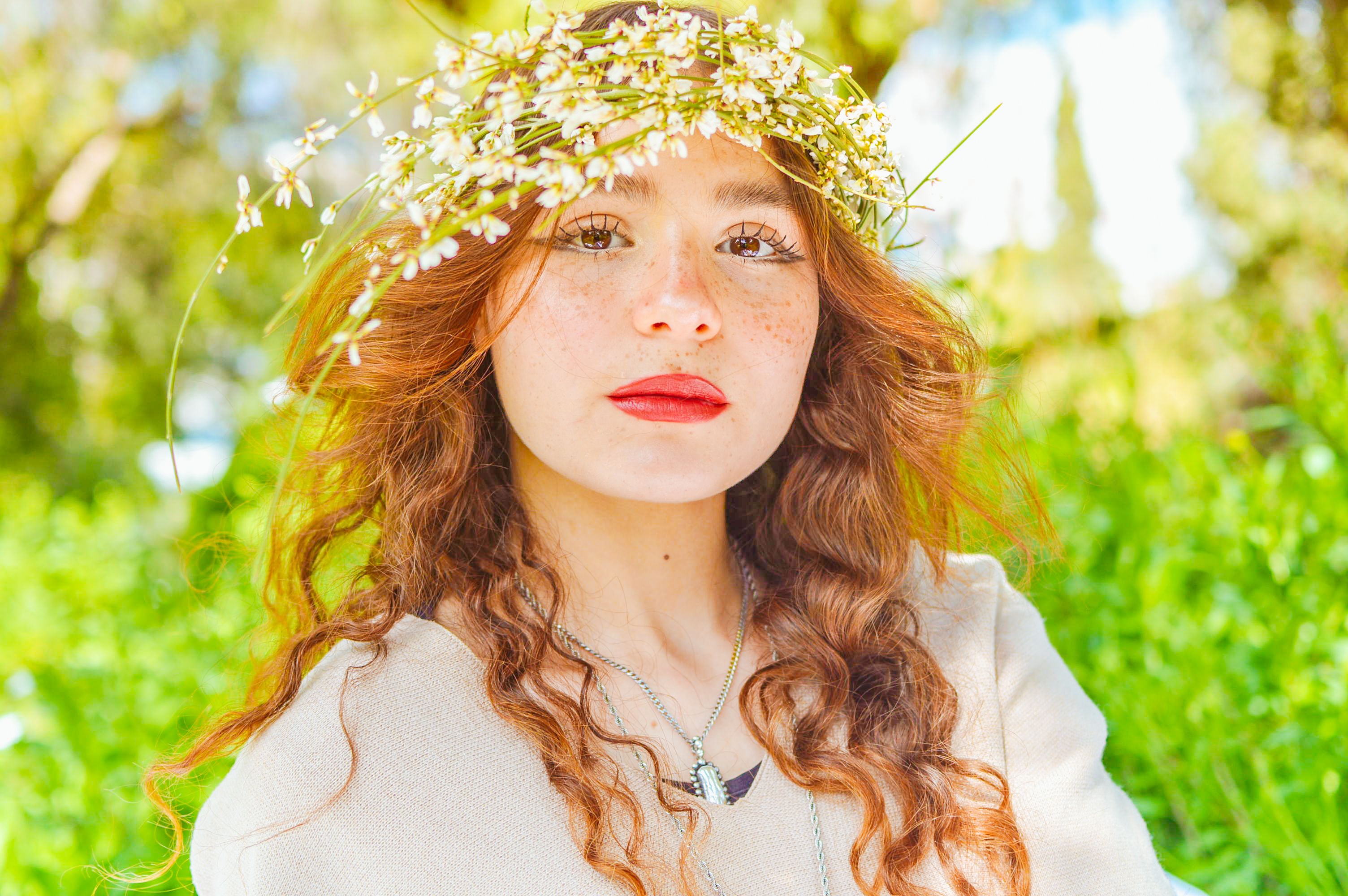 Portrait of a woman with a floral crown, outdoors in vibrant sunlight.