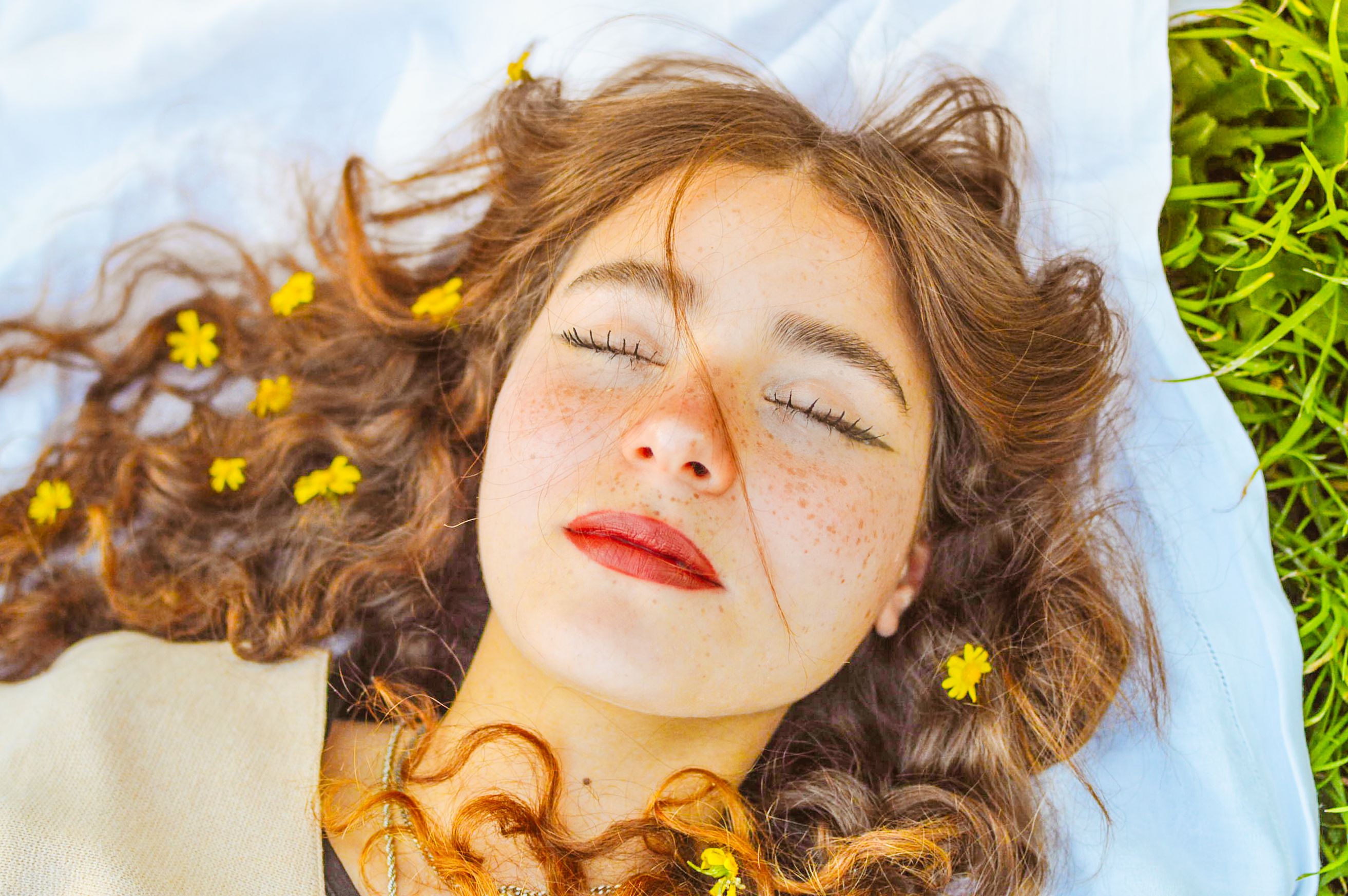 Peaceful woman with flowers in hair lying on grass, eyes closed.