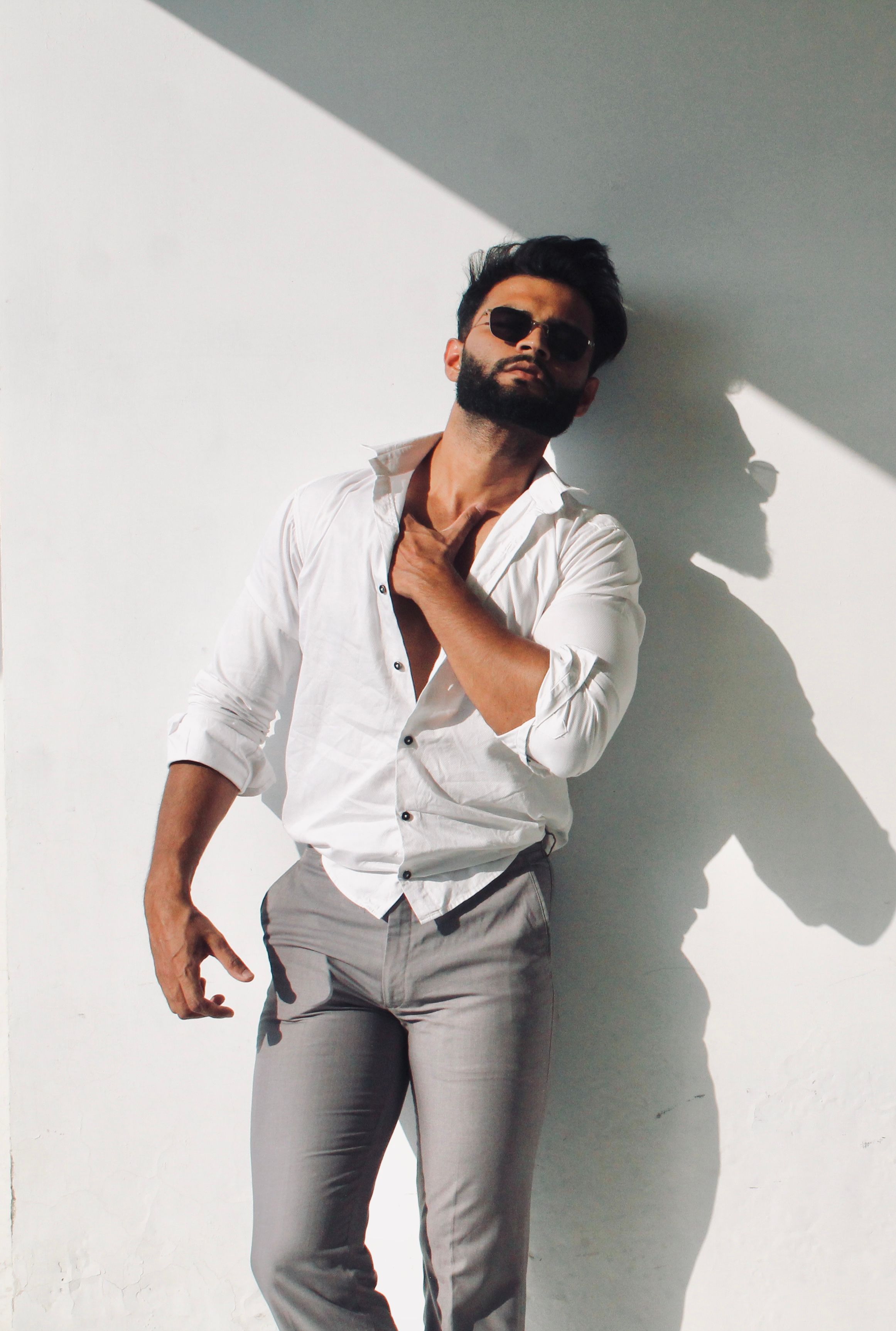 Confident man in white shirt poses boldly against a wall with dramatic lighting and shadows.